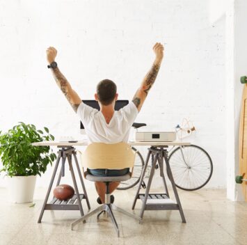 Freelance tatoué levant les bras en signe de victoire devant son bureau - optimiser votre profil freelance